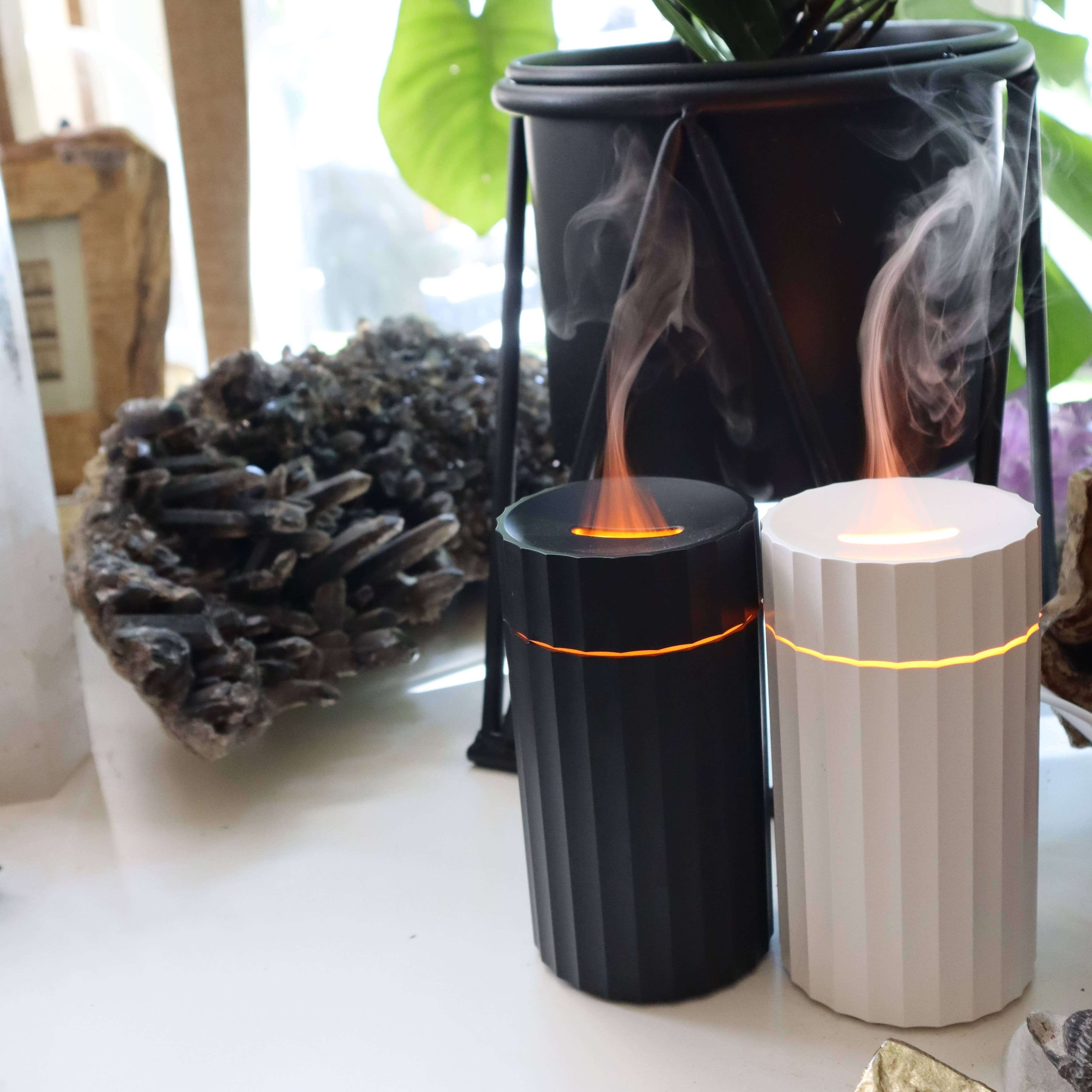 Mini multi-color flame essential oil diffusers in black and white with aromatic smoke, enhancing home ambiance.